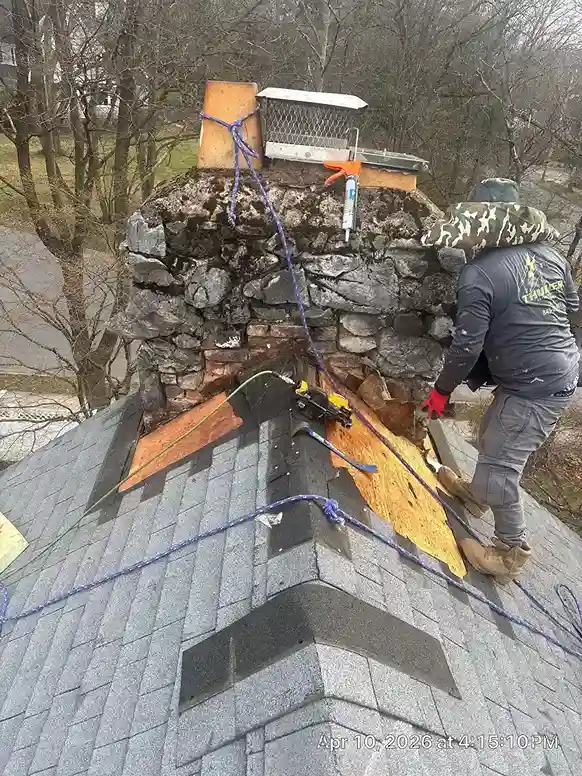 Roofer applying sealant to stone chimney flashing